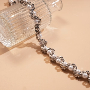 Detailed close-up of faux pearl and metallic twisted chain necklace on glass accessory