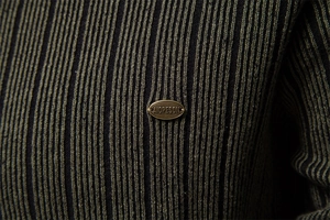 Detailed macro view of dark green and black striped knit fabric with metal brand logo