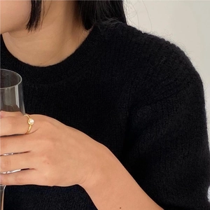 Close-up of a gold pearl ring worn by a model holding a glass against a black knit sweater