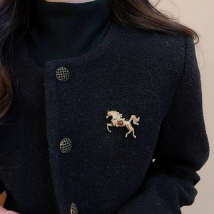 Close-up of golden horse brooch with red gemstone on black tweed jacket for elegant look