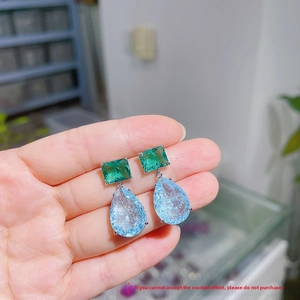 Detail of double-layer earrings with green square gem and blue teardrop cracked stone