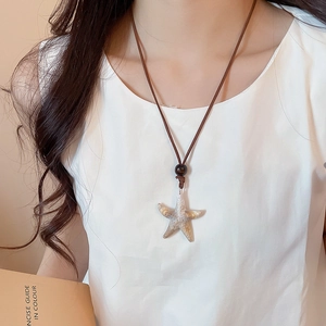 Detail of white starfish pendant necklace with brown cord on a model with neutral background