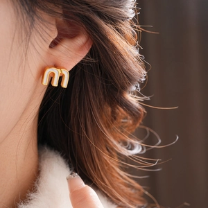 Close-up of golden letter M earrings with white enamel detail worn by a model