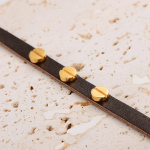 Vista macro di bracciale in pelle marrone scuro con tre borchie dorate a forma di vite