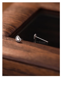 Macro shot of silver heart stud earrings with polished finish on a dark wooden frame