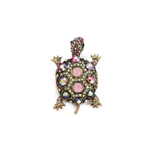 Vintage gold turtle brooch with pink and blue rhinestones on a white background