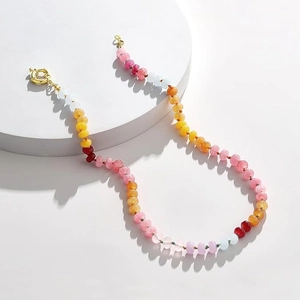 Detail of colorful crystal beaded necklace with natural stones and golden clasp on white pedestal