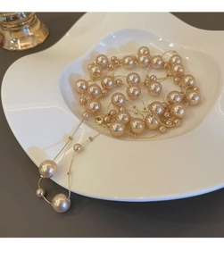 Détail d'un collier de perles champagne avec maillons dorés sur un plateau céramique