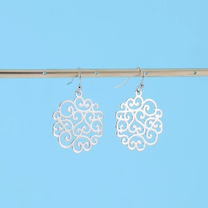 Close-up of silver hollowed-out filigree drop earrings hanging on a gold metal stand