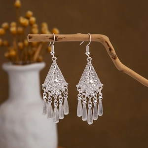 Detailed close-up of retro silver drop earrings with peacock-style fringes on wooden branch