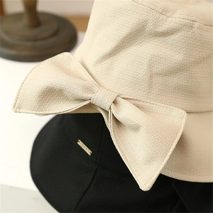 Close-up of beige bow and black hat texture with metal tag on knit fisherman hats