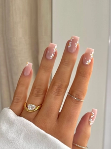 Close-up of long rectangular nude pink press-on nails with white daisy floral designs