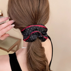 Rear view of a model wearing a large black polka dot fabric scrunchie with red piping