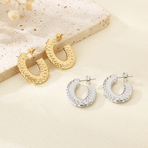 Detail of C-shaped stainless steel earrings with textured fish scale pattern in gold and silver