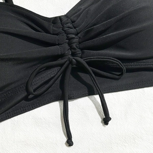 Detail of black swimwear top featuring adjustable drawstring ruching and textured fabric
