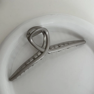 Close-up of silver metal hair claw clip with twisted streamlined design in a white tray