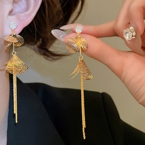 Détail macro de boucles d'oreilles dorées à pompons et zircons sur modèle