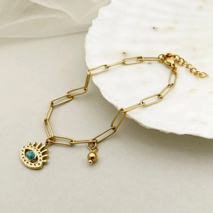 Gold evil eye bracelet with turquoise stone and oval links on a white shell