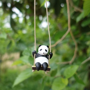 Close-up of a cute panda figurine on a wooden swing with natural green garden background