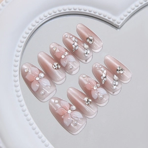 Pink cat eye press-on nails with 3D floral petals, pearls, and crystals on a mirror