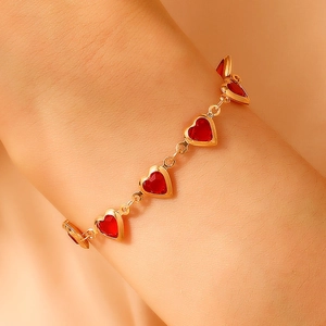 Golden bracelet with red heart charms displayed on a wrist in a warm aesthetic setting