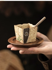 Close-up of hand holding a handmade ceramic daisy cup with wooden tray and spoon set