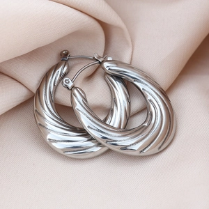 Macro detail of silver twisted hoop earrings resting on light apricot silk fabric