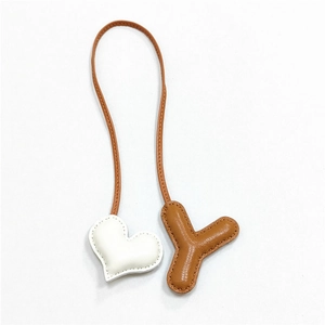 Dettaglio di un ciondolo per borsa in pelle fatto a mano con cuore bianco e lettera Y marrone