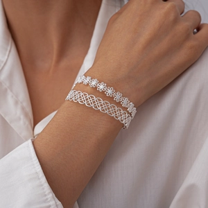 Detail of silver clover flower and hollow mesh cuff bracelets worn on a model's wrist
