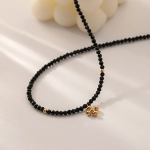 Minimalist black beaded cross necklace with golden flower pendant on soft cream background
