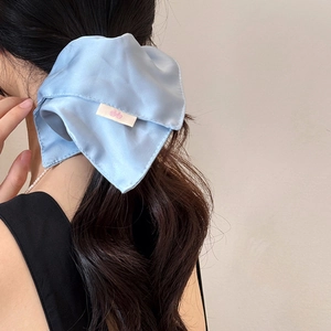 Close-up of light blue satin scrunchie on dark hair showing soft fabric texture