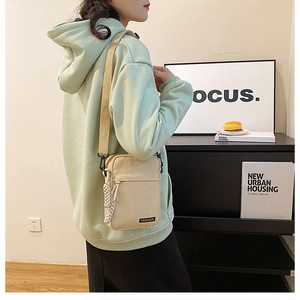 Detail of a cream canvas crossbody bag with zip pocket and woven rope zipper pull