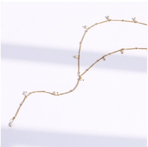 Detail of a thin gold chain necklace with multiple white pearls on a minimalist white background