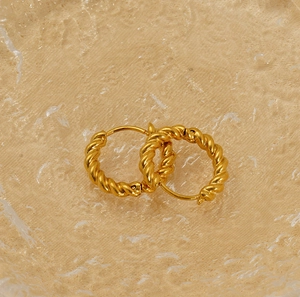 Close-up of 18K gold-plated twisted hoop earrings on a textured gold display tray