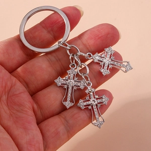 Handheld silver cross keychain featuring sparkling rhinestones on a pink background