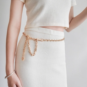 Detail of gold metal chain belt with sun pendant over white textured fabric