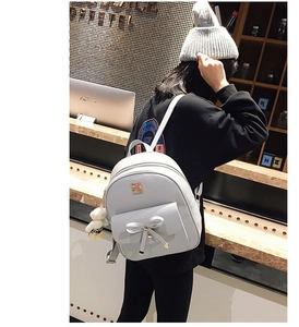 Rear view of a light gray bow-knot backpack with a plush bear charm in a cafe setting