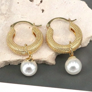 Close-up of golden textured hoop earrings with elegant white pearl drop pendants