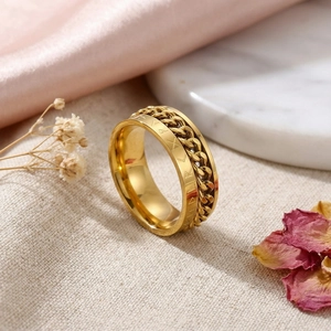 Gros plan d'une bague chaîne dorée avec gravure sur tissu beige et soie rose