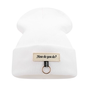 Détail du bonnet blanc à côtes avec écusson lettré et anneau métallique tendance