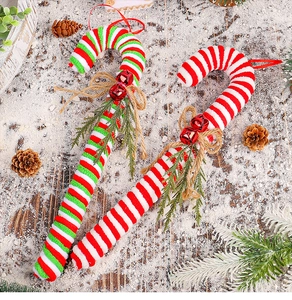 Close-up of candy cane ornaments with red bells, bows and pine needles on snow