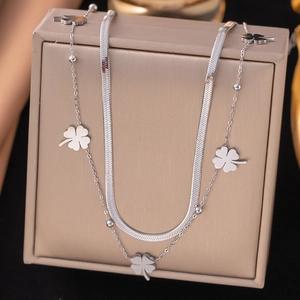 Close-up of silver double-layered flat snake chain necklace with clover pendant on box