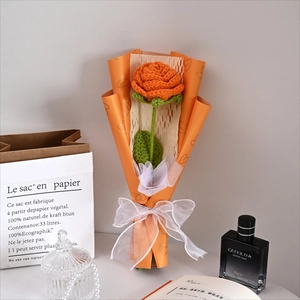 Detailed view of a handmade knitted orange rose bouquet with white chiffon ribbon bow