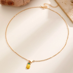 Dettaglio della collana dorata con ciondoli a forma di cuore e ananas in smalto