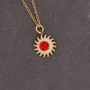Macro shot of sunburst pendant with red gemstone on golden chain against stone