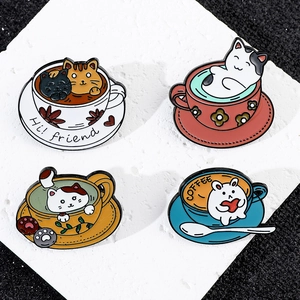 Set of four cute cartoon cat coffee cup enamel brooches displayed on white stone
