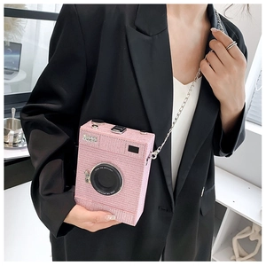 Pink retro camera crossbody bag with silver chain strap shown on a black suit blazer