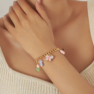 Détail d'un bracelet doré avec des breloques fleurs et papillons en émail coloré au poignet