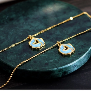 Detail of gold fishtail pendant with blue enamel on green marble surface