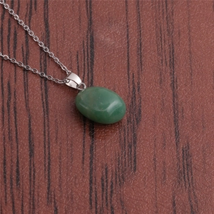 Close-up of a green oval stone pendant with silver chain on a dark wood background